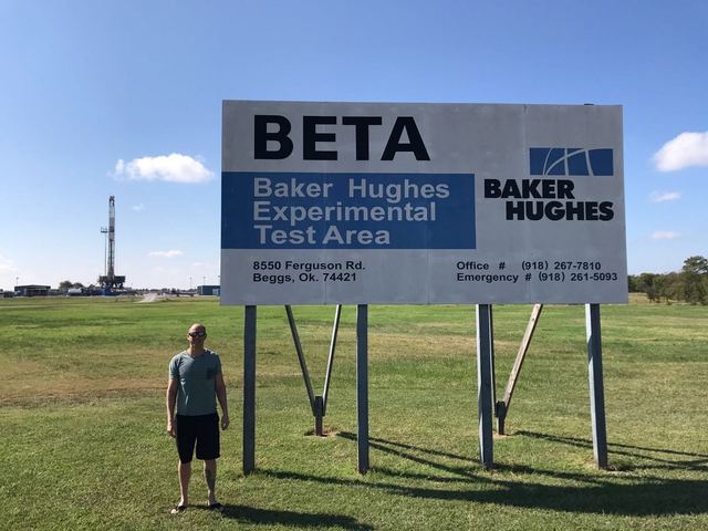 Graham Farmer at the Baker Hughes Experimental Test Area sign with a rig behind