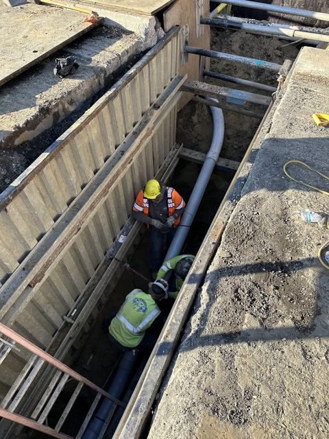 Crew members installing conduit inside a shored utility trench