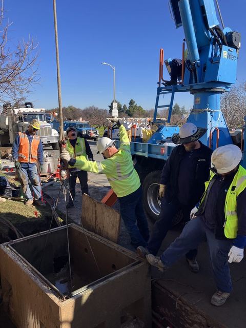 Hard-hatted crew setting an underground splice box beside a crane truck
