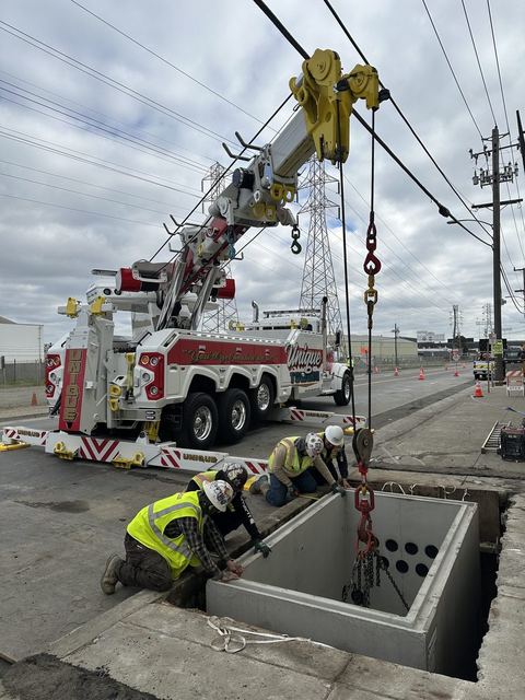 Crew guiding a precast underground vault into place with a boom truck